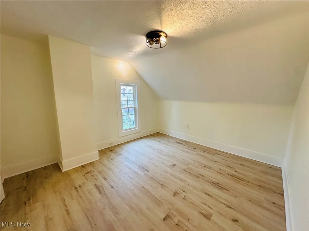 Bonus room featuring lofted ceiling, light wood-style flooring, and a textured ceiling