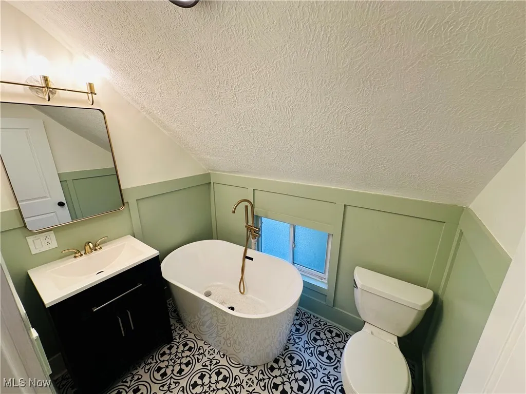 Bathroom featuring vanity, a soaking tub, a textured ceiling, a decorative wall, and lofted ceiling