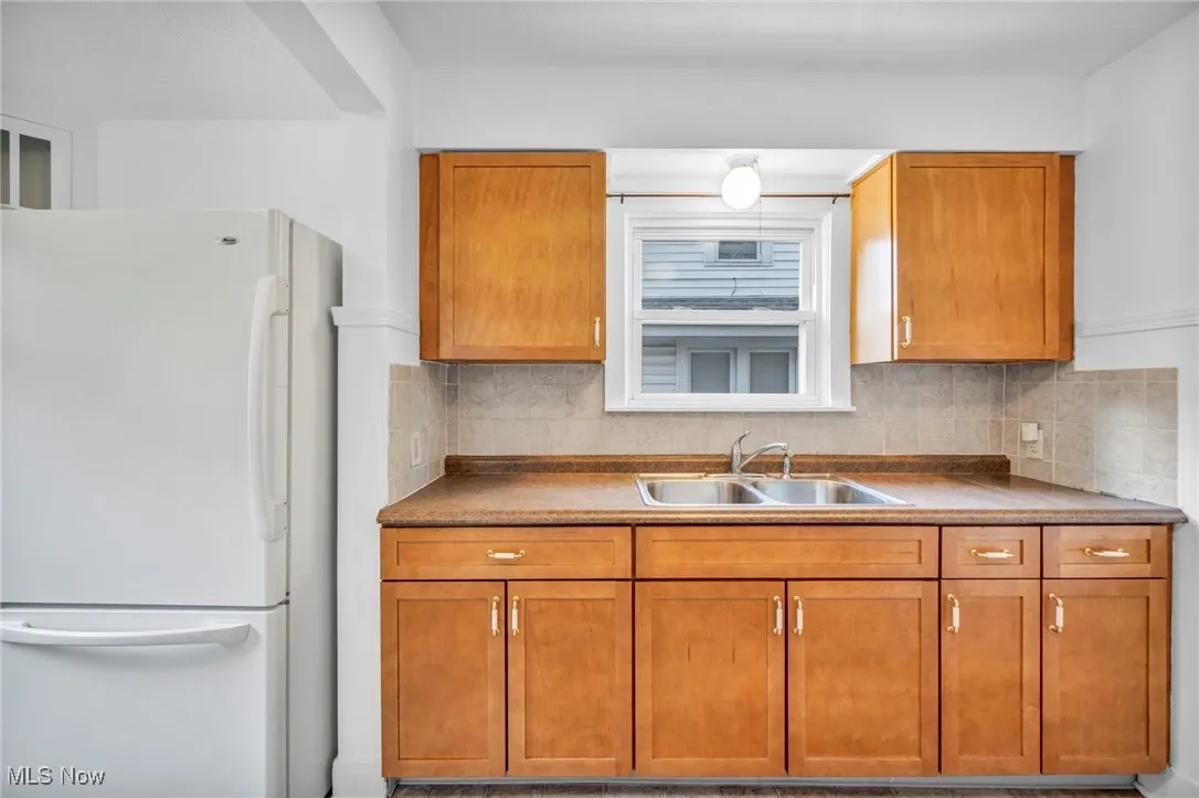 Kitchen featuring freestanding refrigerator, brown cabinets, tasteful backsplash, and dark countertops