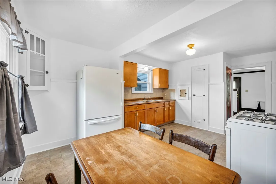 Kitchen featuring brown cabinets, white appliances, light countertops, decorative backsplash, and light tile patterned floors
