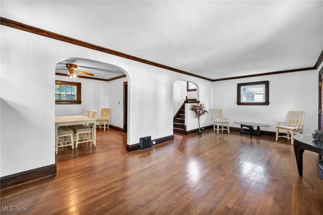 Living room featuring arched walkways, crown molding, dark wood-style flooring, stairway, and plenty of natural light