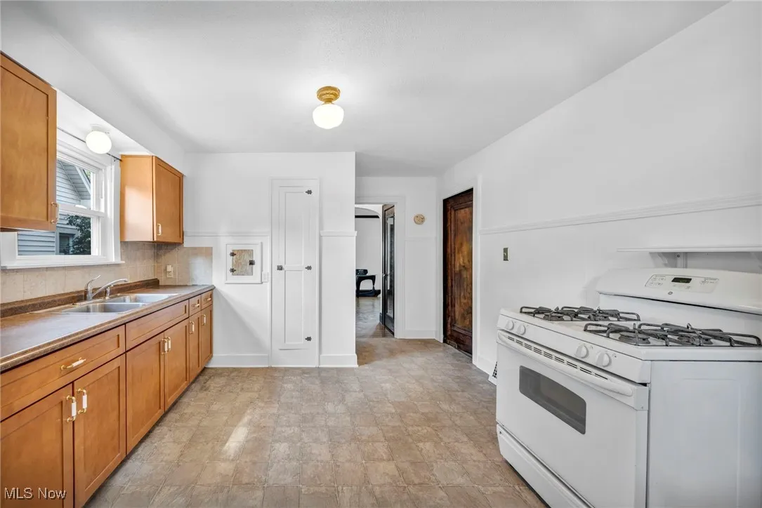 Kitchen with white gas stove, brown cabinets, decorative backsplash, and dark countertops