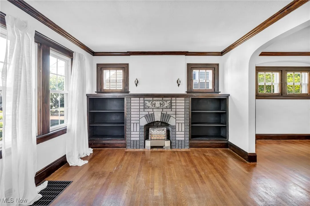 Unfurnished living room featuring arched walkways, a brick fireplace, crown molding, and hardwood / wood-style flooring