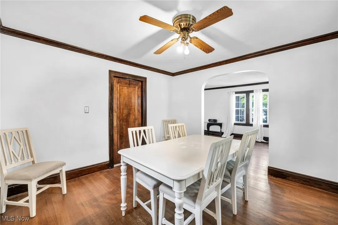 Dining area with ornamental molding, arched walkways, dark wood-type flooring, and a ceiling fan