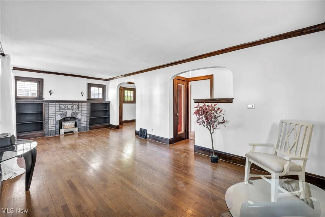 Living area featuring ornamental molding, arched walkways, dark wood-type flooring, and a fireplace