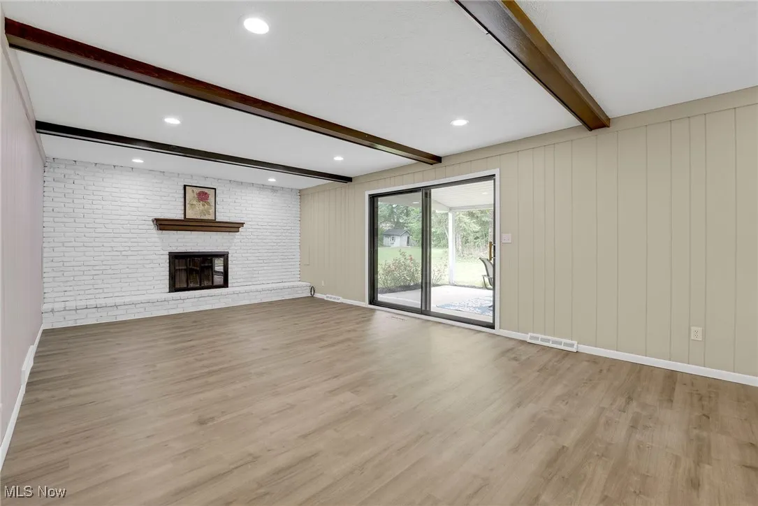 Large family room with a beamed ceiling, brick-accented fireplace, and oversized sliding doors to the covered patio