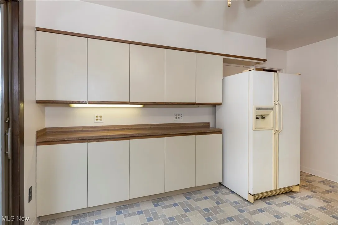 Kitchen with white refrigerator with ice dispenser, counters, and white cabinetry