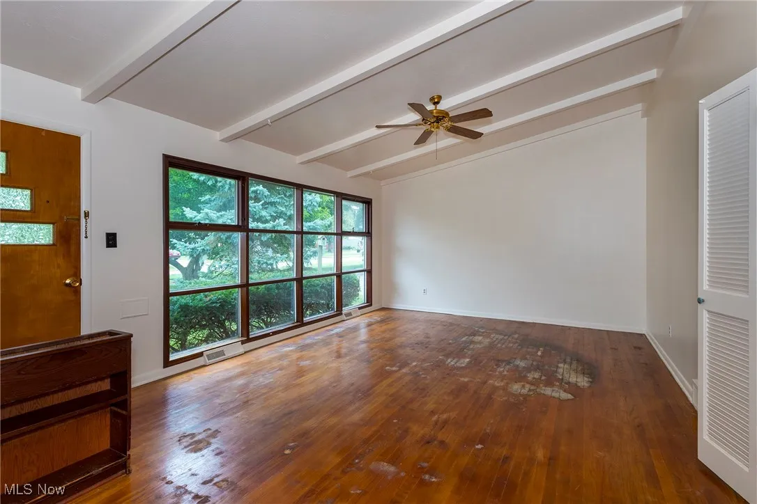 Unfurnished living room with hard wood floors, beamed ceilings and a ceiling fan