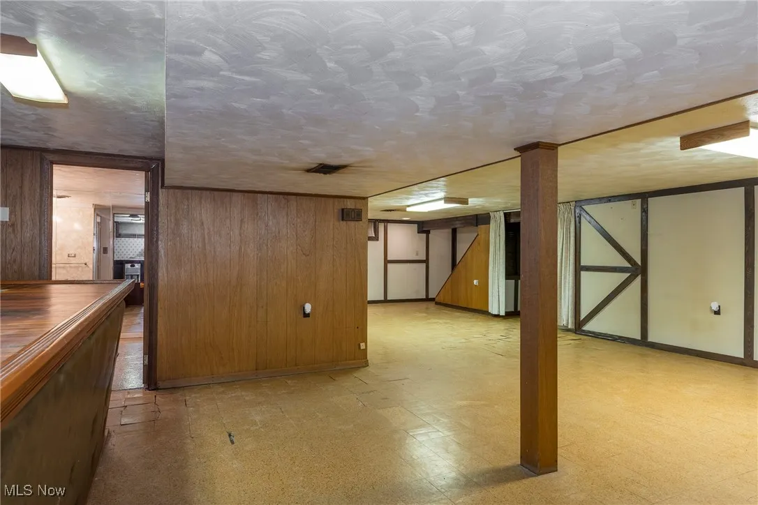 Finished basement with light floors and wooden wall accents - view from bar area