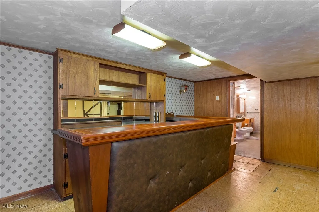 Bar with light floors, wallpapered walls, brown cabinets, open shelves, and dark countertops