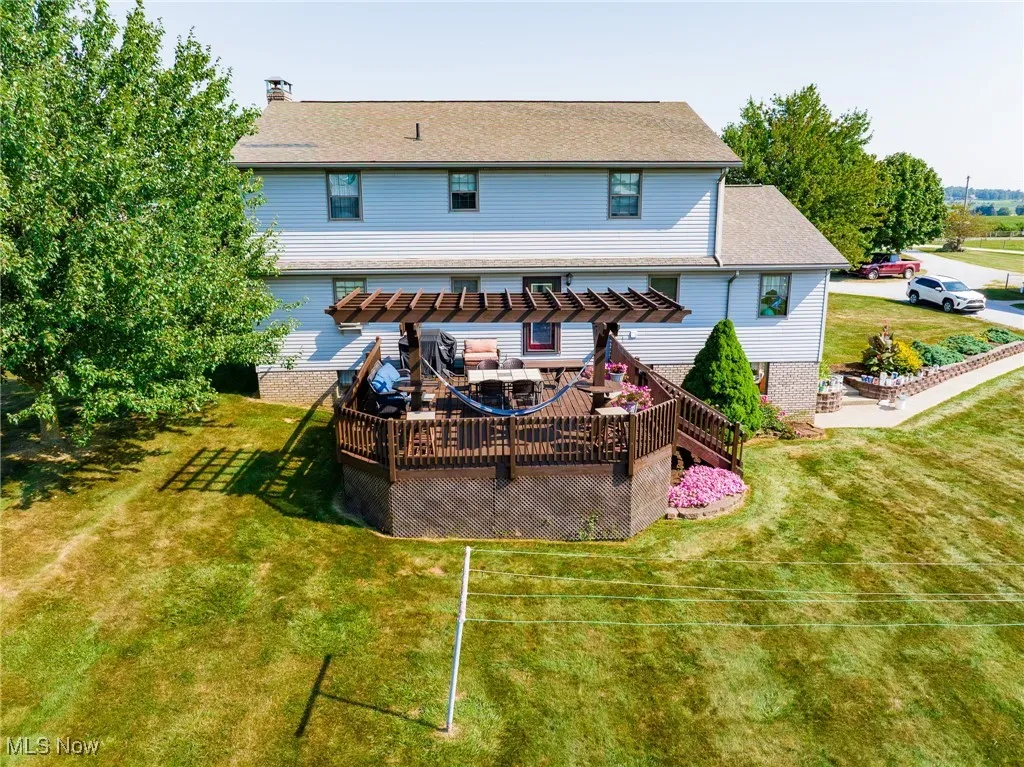 Back of house with a deck, a lawn, a pergola, a shingled roof, and a chimney