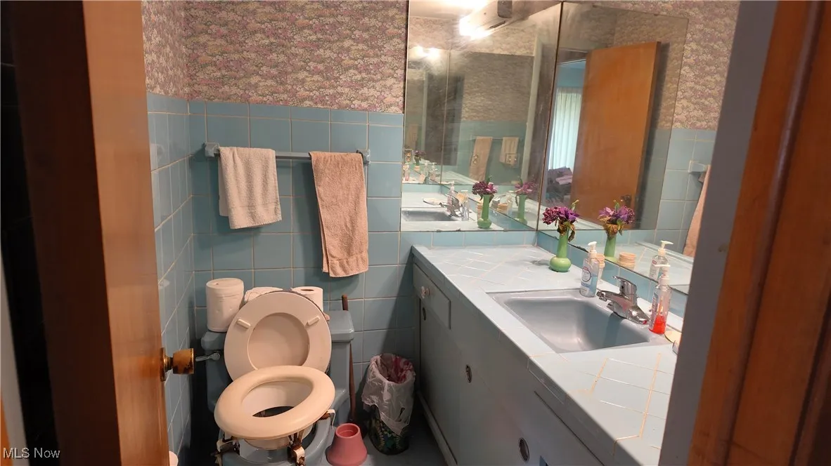 Bathroom featuring tile walls, wallpapered walls, vanity, and a wainscoted wall