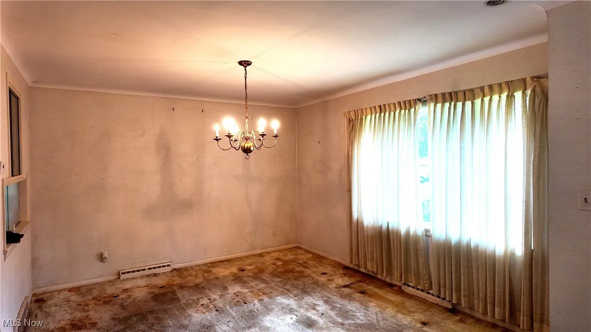 Unfurnished dining area with a chandelier and baseboards