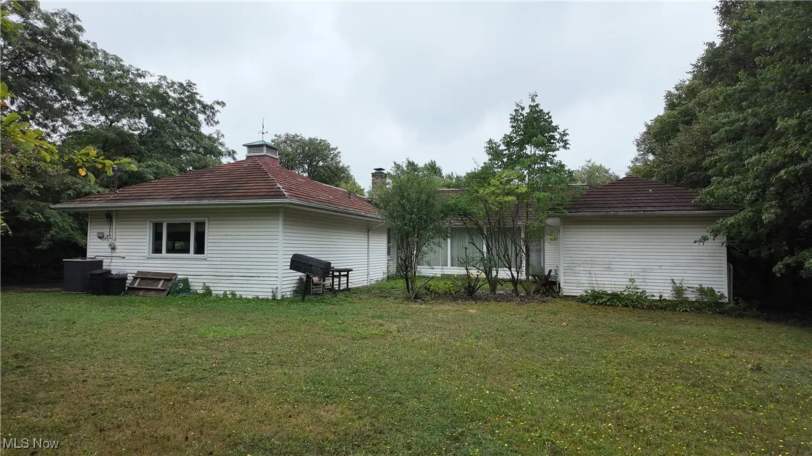 Rear view of property featuring a lawn, a chimney, and a tile roof