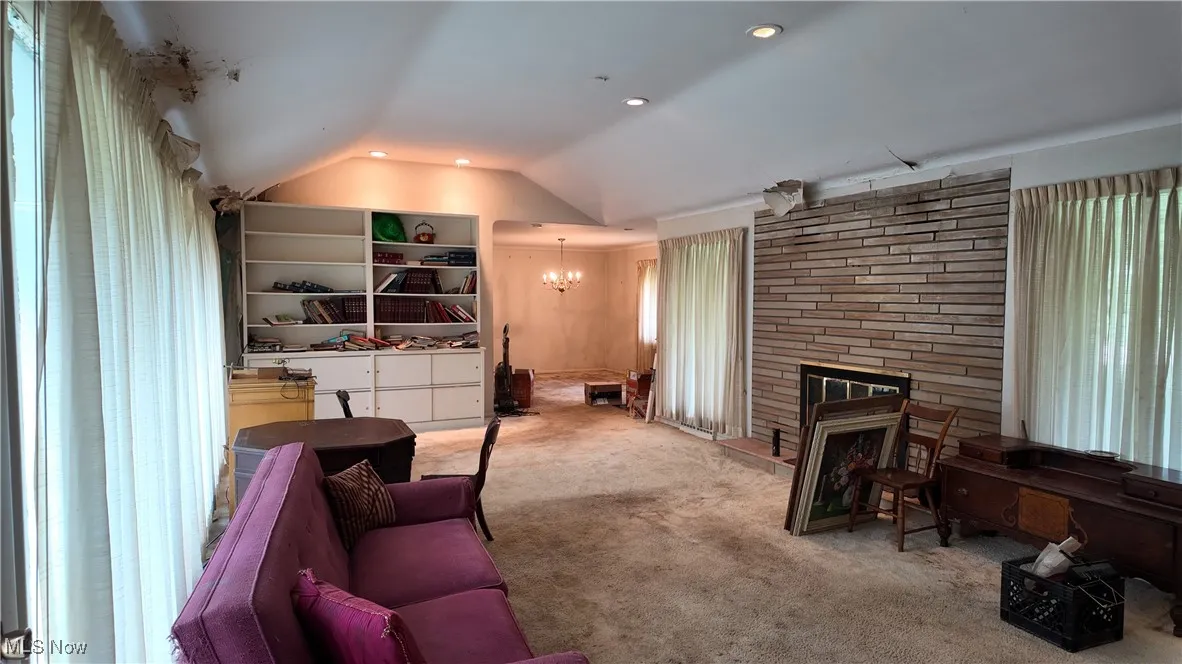 Living room with vaulted ceiling, carpet floors, a stone fireplace, a chandelier, and recessed lighting