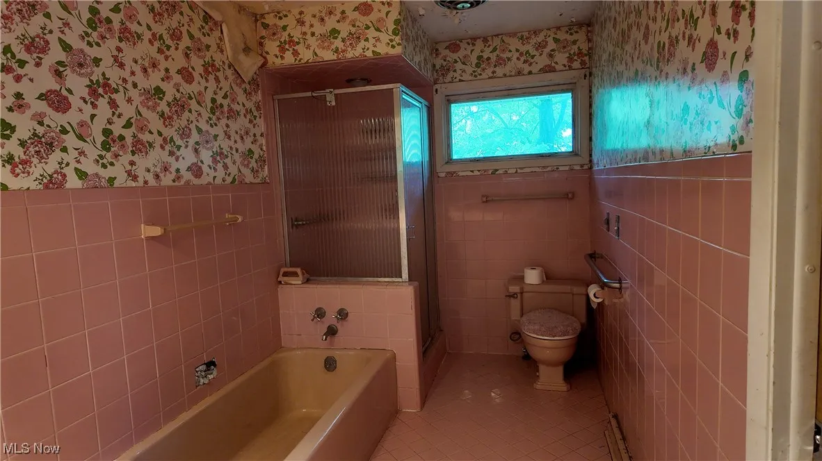Bathroom with light tile patterned floors, tile walls, a stall shower, wainscoting, and a garden tub