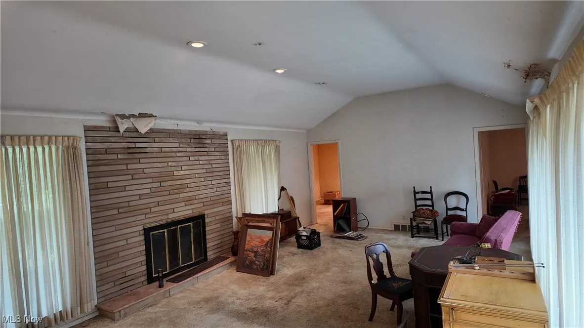 Carpeted living room featuring vaulted ceiling and a fireplace