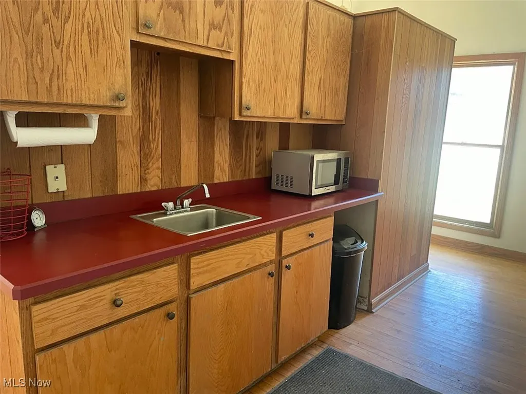 Kitchen featuring dark countertops, stainless steel microwave, light wood-type flooring, wood walls, and brown cabinetry