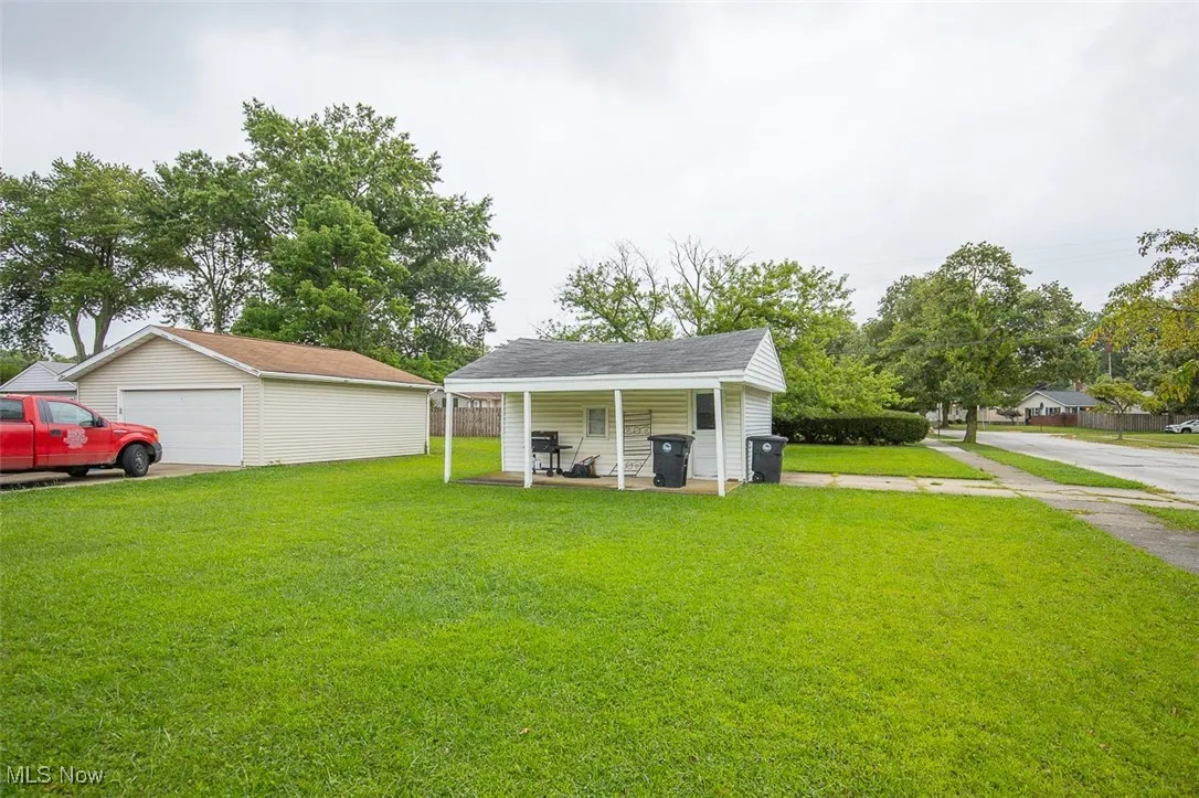 View of grassy yard featuring an outdoor structure, covered porch, and a detached garage