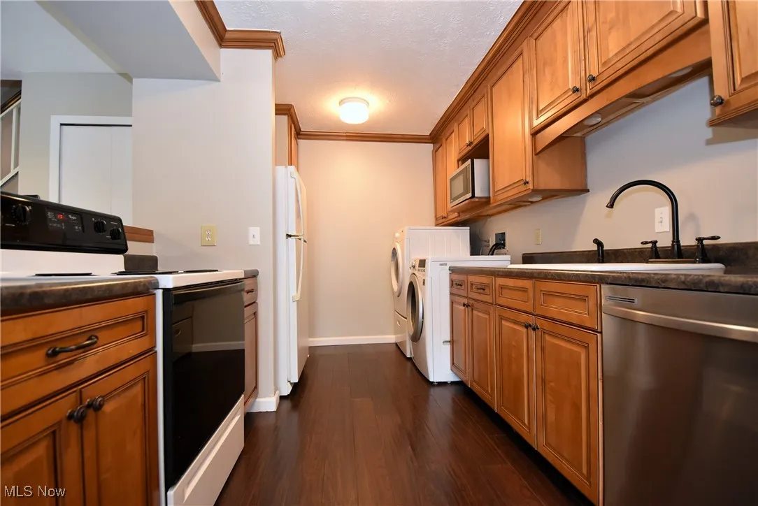 Kitchen featuring stainless steel appliances, brown cabinets, a textured ceiling, dark wood-type flooring, and crown molding