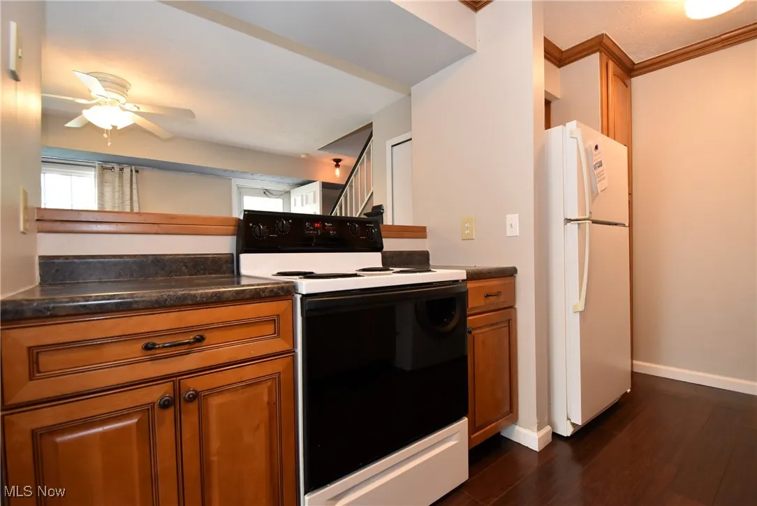 Kitchen with white appliances, dark countertops, brown cabinets, crown molding, and dark wood-type flooring