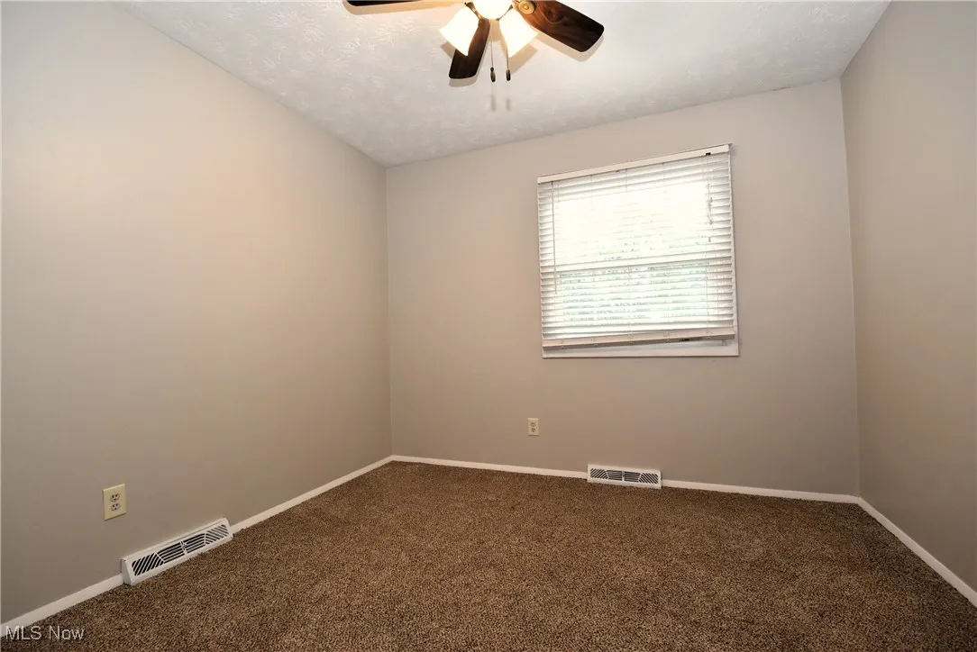 Unfurnished room featuring dark carpet, a textured ceiling, and ceiling fan