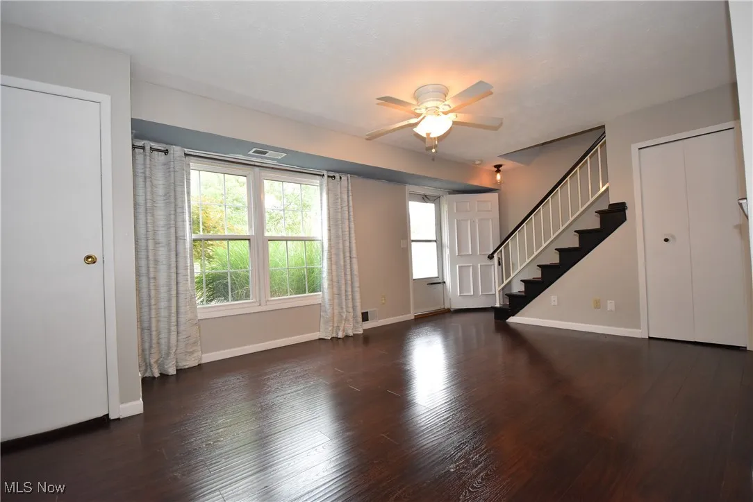 Unfurnished living room with dark wood-style floors, ceiling fan, and stairway