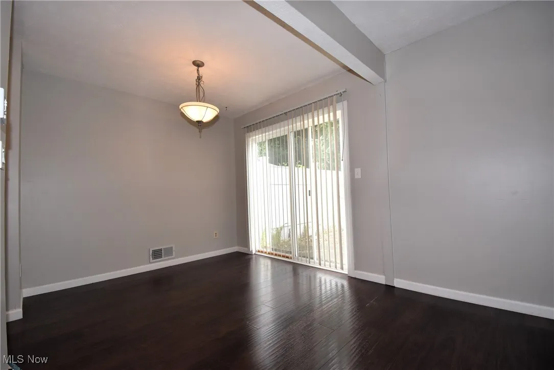 Spare room featuring dark wood-type flooring and beamed ceiling