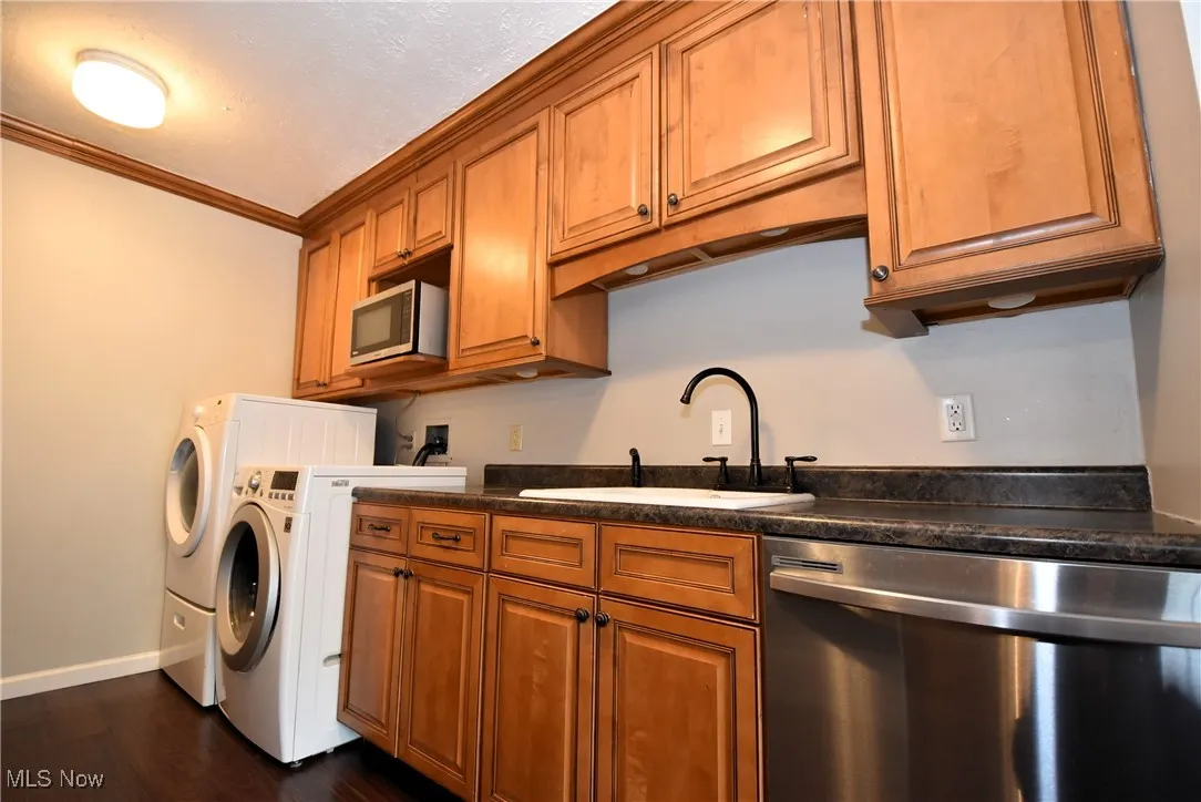 Kitchen with stainless steel appliances, brown cabinets, ornamental molding, dark wood-style flooring, and washer and dryer