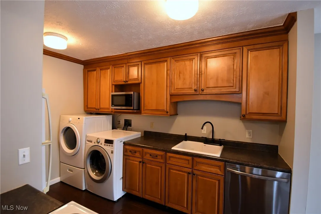 Kitchen with brown cabinetry, stainless steel appliances, a textured ceiling, ornamental molding, and dark wood-style floors