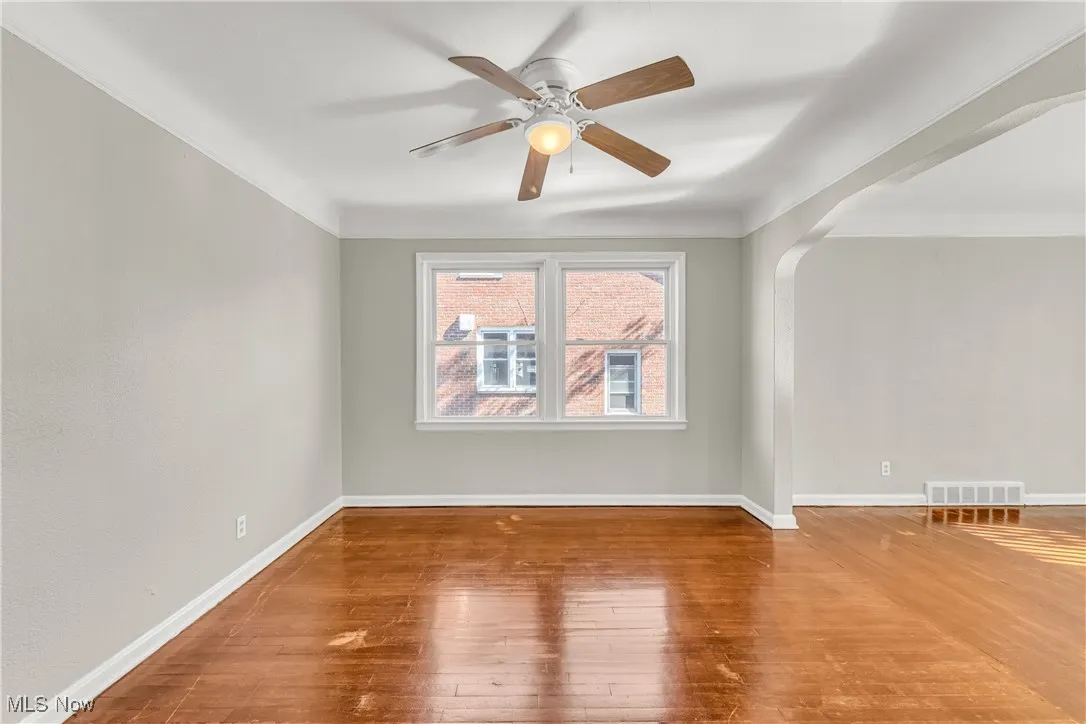 Unfurnished room with arched walkways, hardwood / wood-style floors, ceiling fan, and ornamental molding