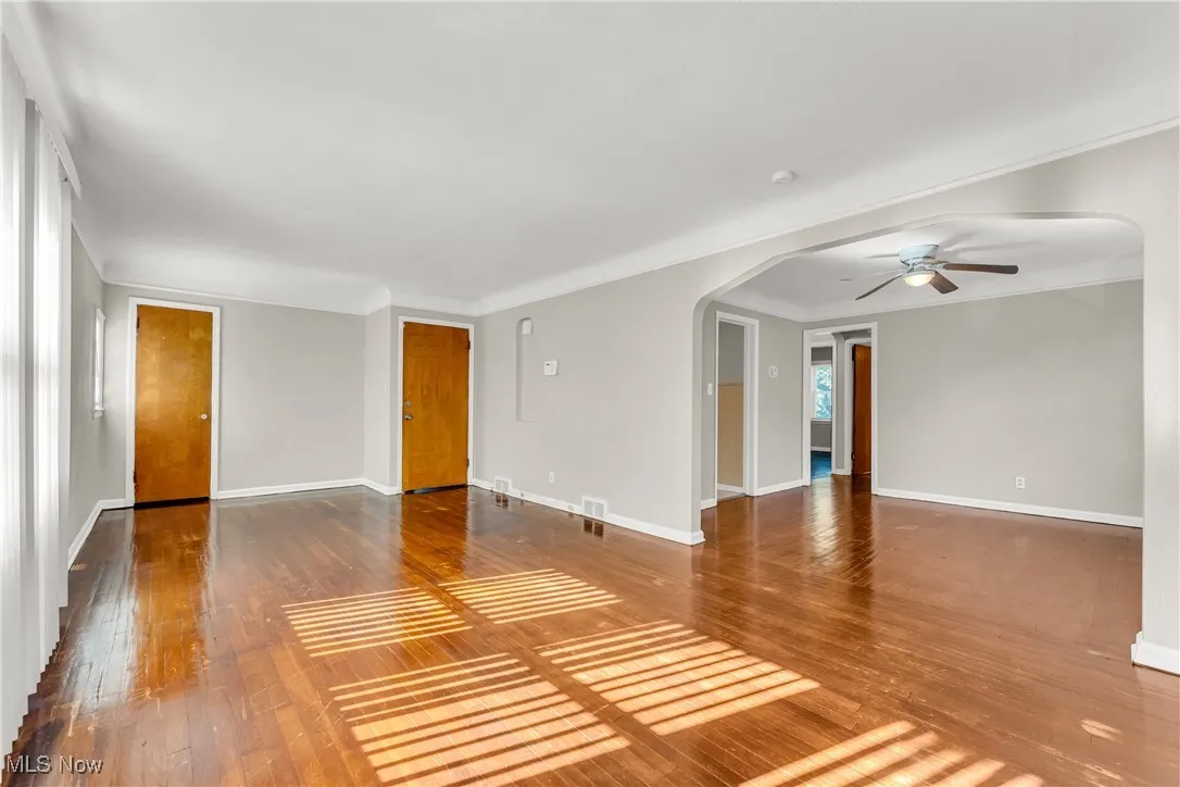Unfurnished living room featuring arched walkways, hardwood / wood-style floors, ceiling fan, and crown molding