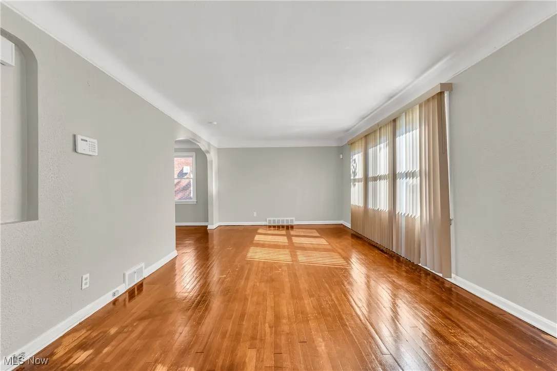 Empty room with arched walkways, a textured wall, and hardwood / wood-style floors