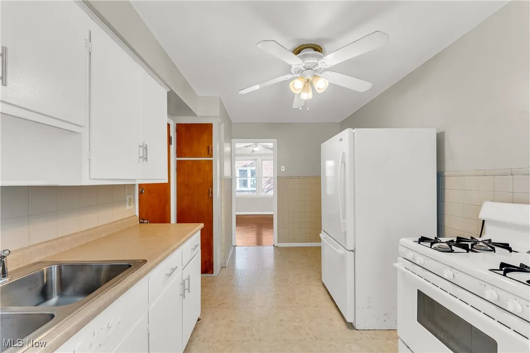Kitchen featuring white appliances, wainscoting, white cabinets, light countertops, and light flooring