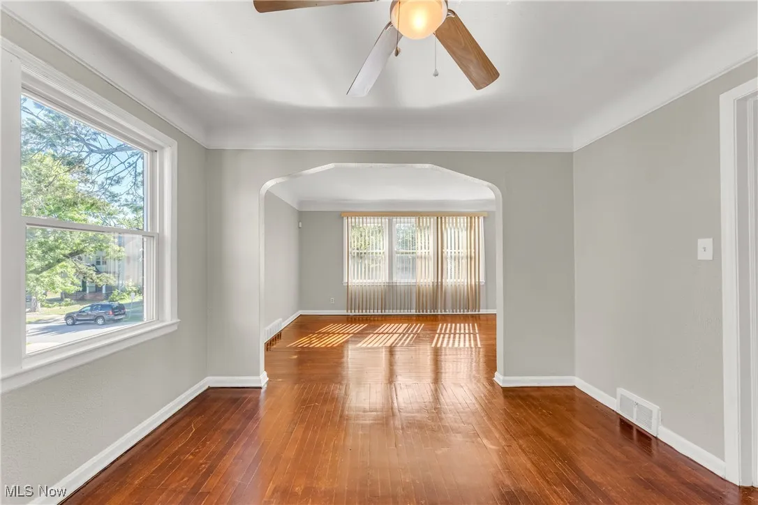 Empty room with dark wood-type flooring, arched walkways, ornamental molding, and ceiling fan