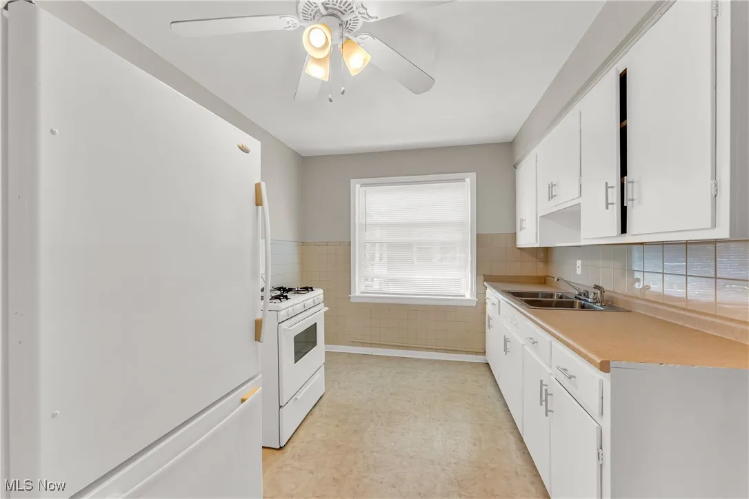 Kitchen featuring white appliances, white cabinetry, light countertops, light floors, and a wainscoted wall