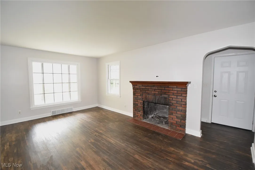 Unfurnished living room featuring arched walkways, a brick fireplace, and dark wood finished floors