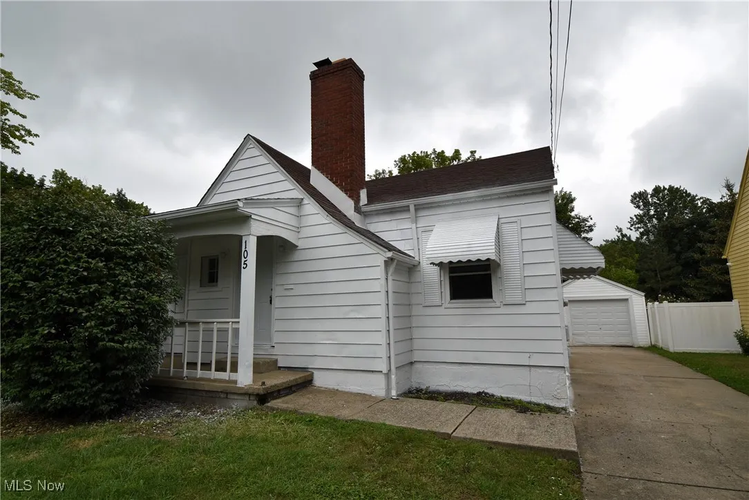 View of front facade with a chimney, an outbuilding, a detached garage, and covered porch