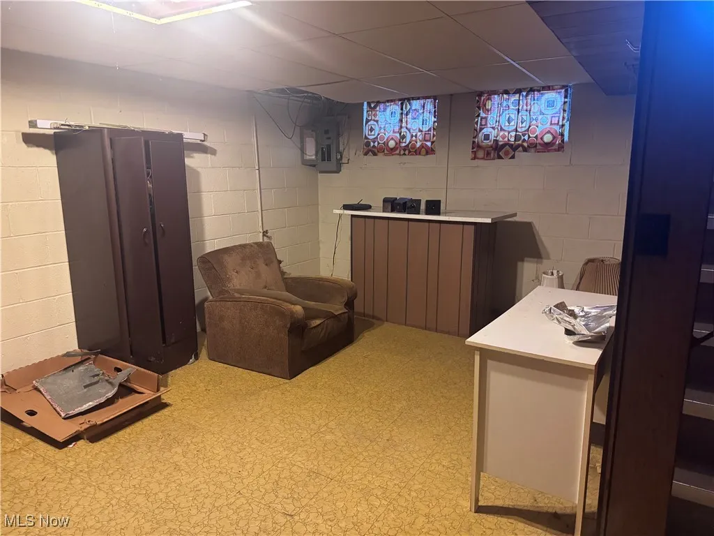 Home office with electric panel, light floors, and a drop ceiling
