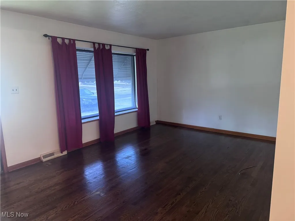 Spare room with dark wood-style flooring and baseboards