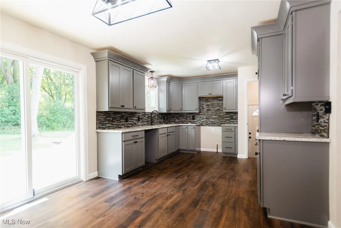 Kitchen with gray cabinetry, backsplash, dark wood-type flooring, and light stone counters