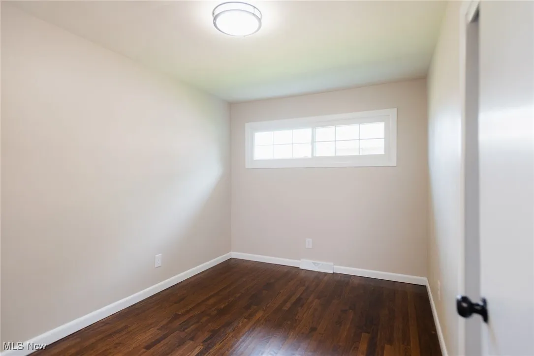 Empty room featuring dark wood-style flooring and baseboards