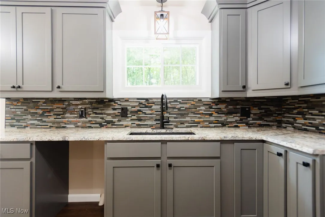 Kitchen featuring gray cabinetry, decorative light fixtures, and light stone countertops