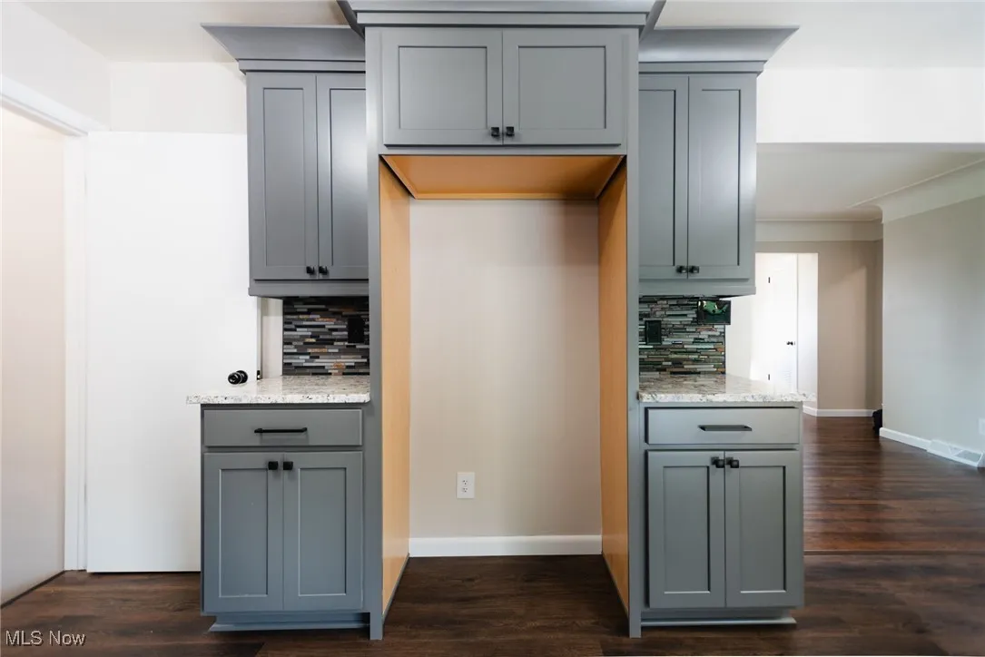 Kitchen featuring gray cabinetry, light stone countertops, dark wood finished floors, and tasteful backsplash