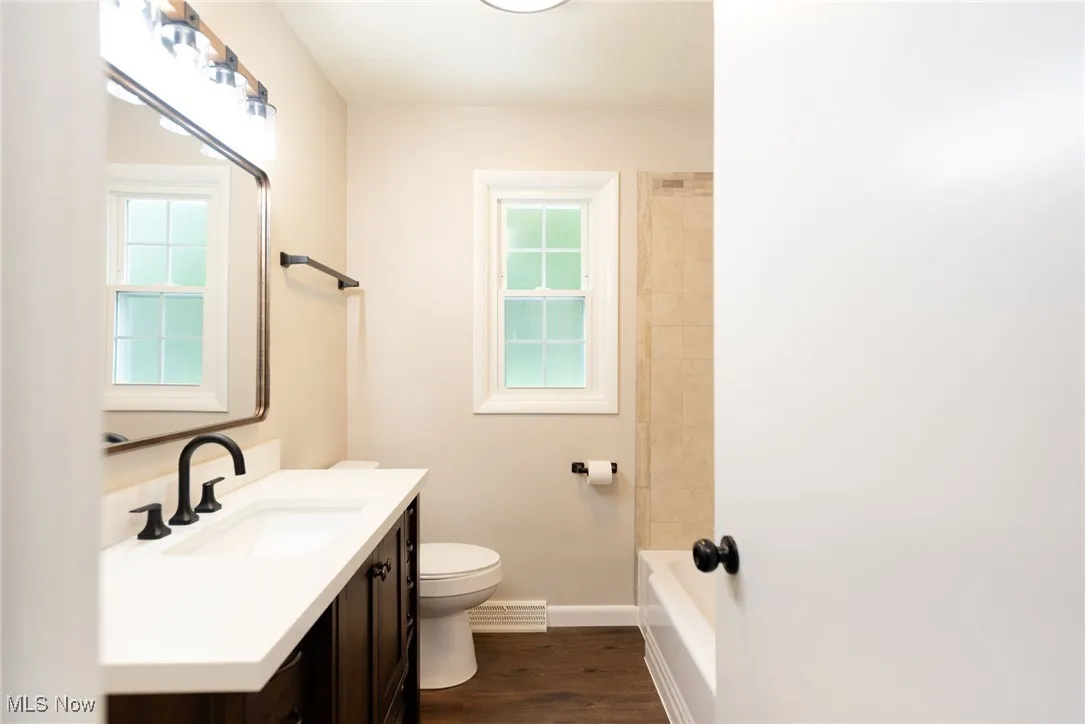 Bathroom with vanity, dark wood-type flooring, shower / washtub combination, and a baseboard radiator