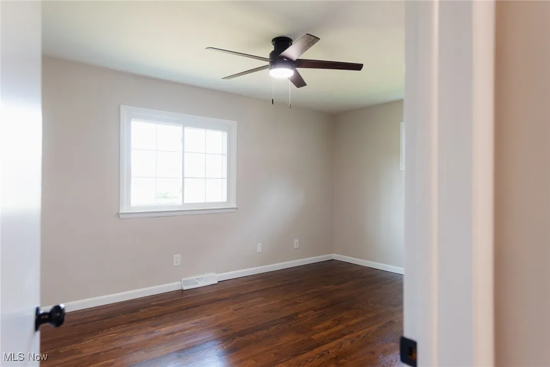 Unfurnished room featuring dark wood-style flooring and a ceiling fan