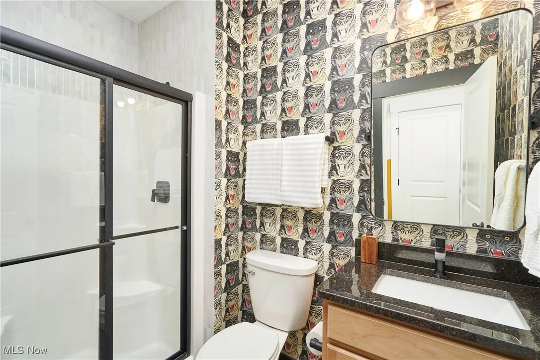 Full bathroom with wallpapered walls, a stall shower, and vanity