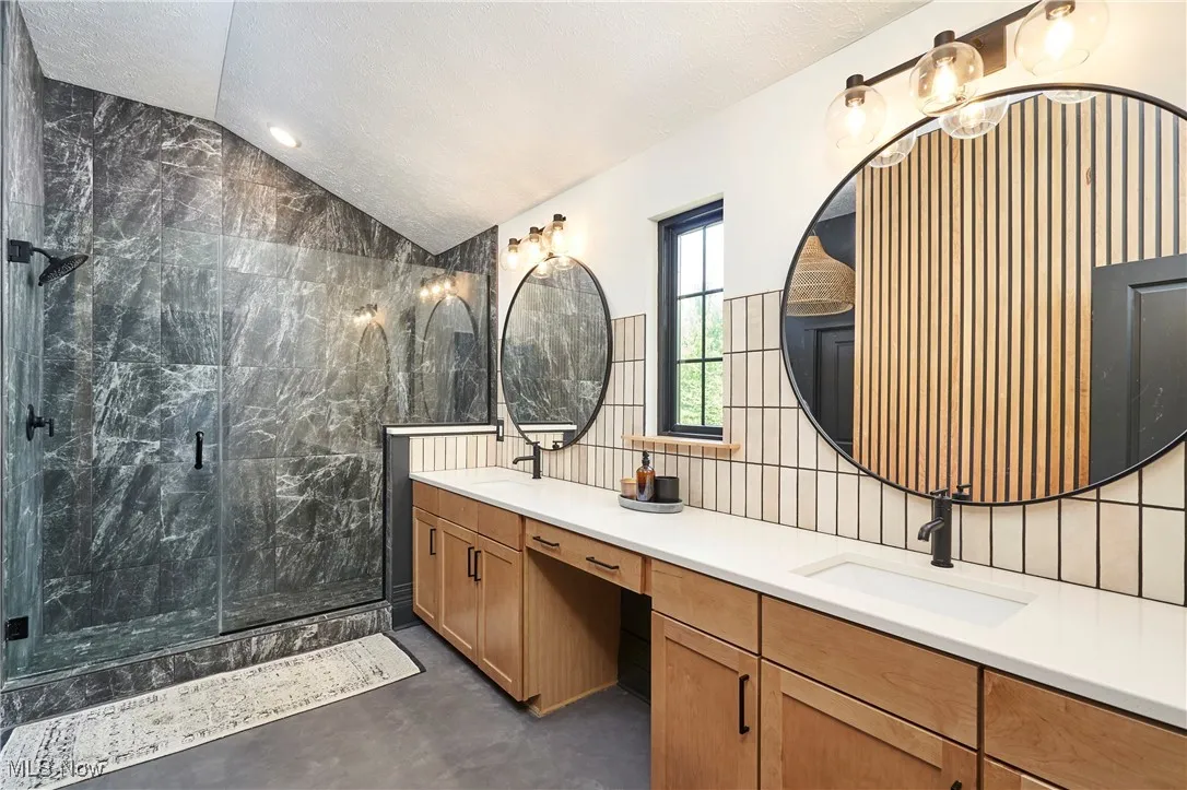 Bathroom with a marble finish shower, double vanity, lofted ceiling, finished concrete flooring, and tile walls