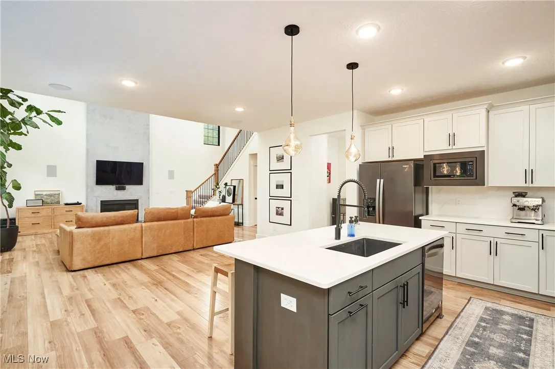 Kitchen with a large fireplace, decorative light fixtures, light wood finished floors, appliances with stainless steel finishes, and gray cabinetry