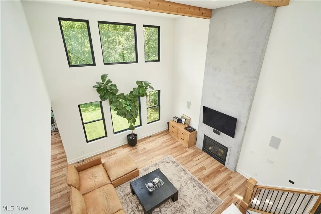 Living room featuring plenty of natural light, beamed ceiling, a fireplace, light wood-style flooring, and a towering ceiling